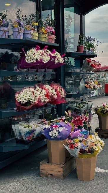 A display of colorful floral arrangements and bouquets at a flower shop, featuring a variety of fresh flowers including white chrysanthemums, pink lilies, purple irises, and mixed seasonal blooms. The